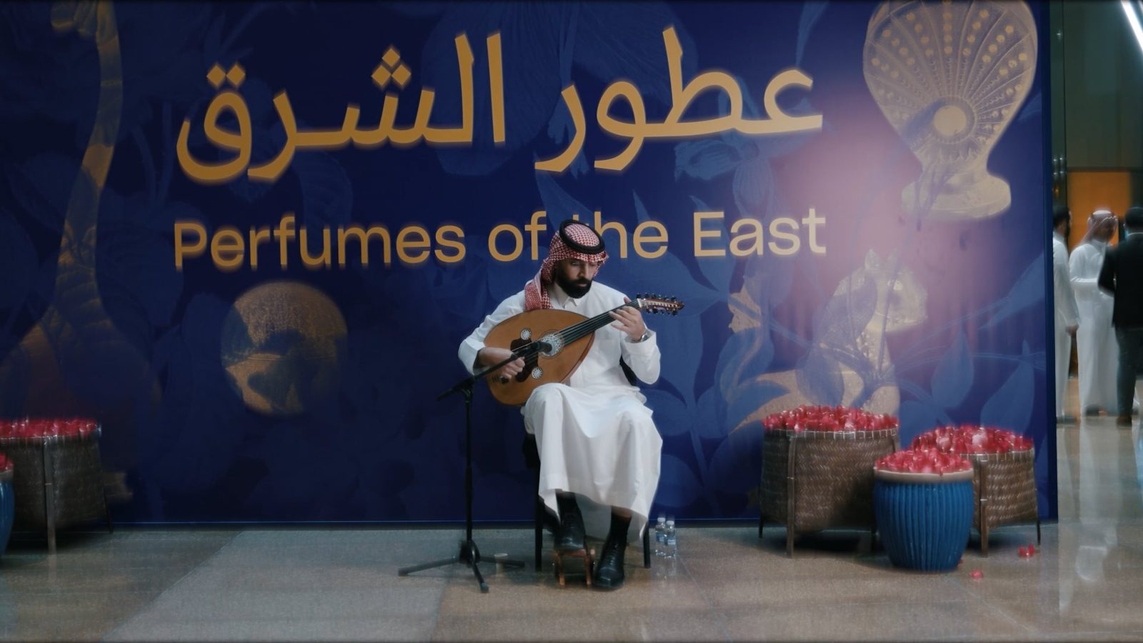 عازف عود أمام لوحة معرض عطور الشرق